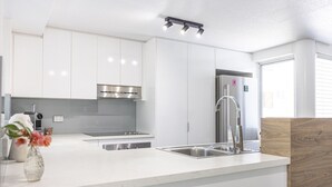 A modern kitchen with white cabinetry, stainless steel appliances, and a central island with a sink. - BeachLuxe @ Sunseeker, Sublime Tropical Apartment (Port Douglas)