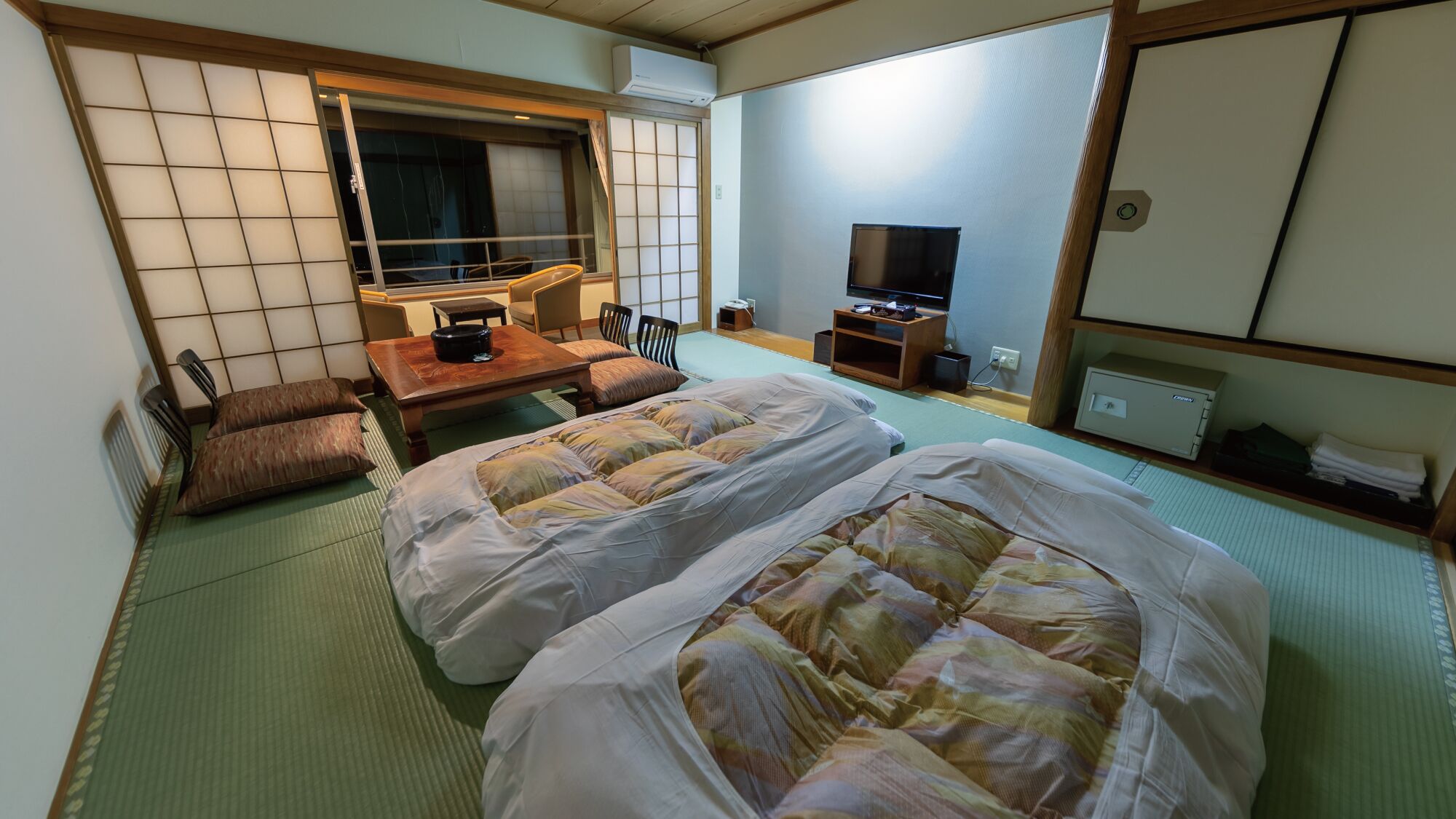 Een traditionele Japanse kamer met tatami vloerbedekking, twee bedden met futons, een televisie, een bureau met stoel en een schuifdeur.
