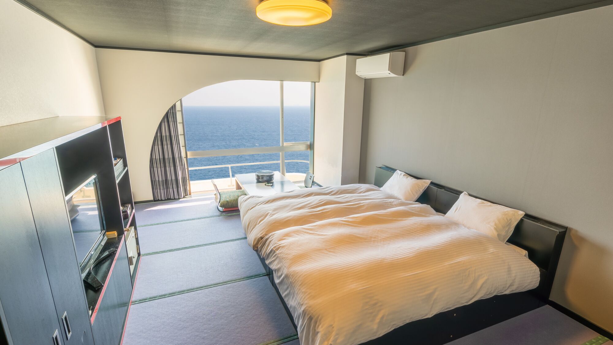 Een slaapkamer met een bed, een bureau en uitzicht op de oceaan.