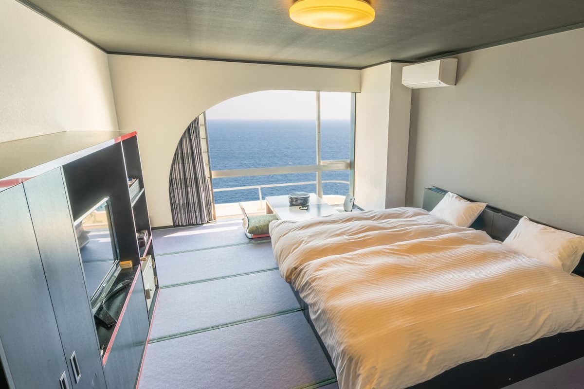 A bedroom with a bed, a desk, and a view of the ocean.