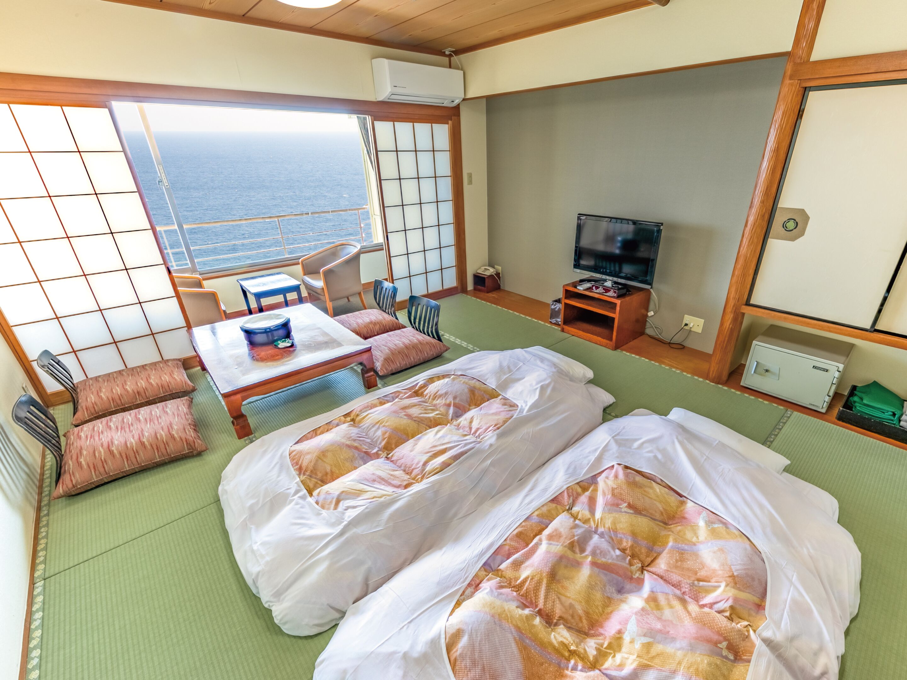A traditional Japanese room with tatami flooring, two beds, a television, and a view of the sea.