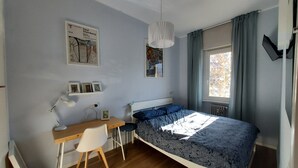 Ett sovrum med en säng, ett skrivbord, en stol, en hängande lampa och ett fönster med gardiner.
