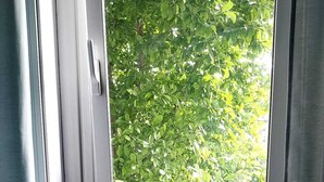 Ett fönster med utsikt över grönt lövverk, ett element under fönstret och ett papper med text på en mönstrad yta.
