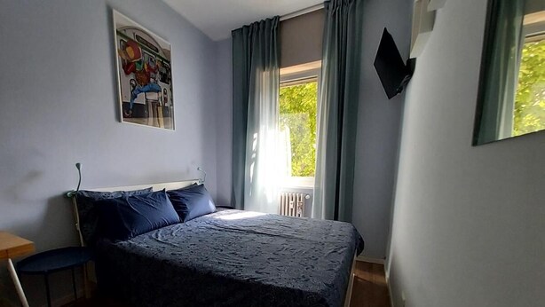 Ett sovrum med en säng, en stol, ett skrivbord och ett fönster med gardiner.