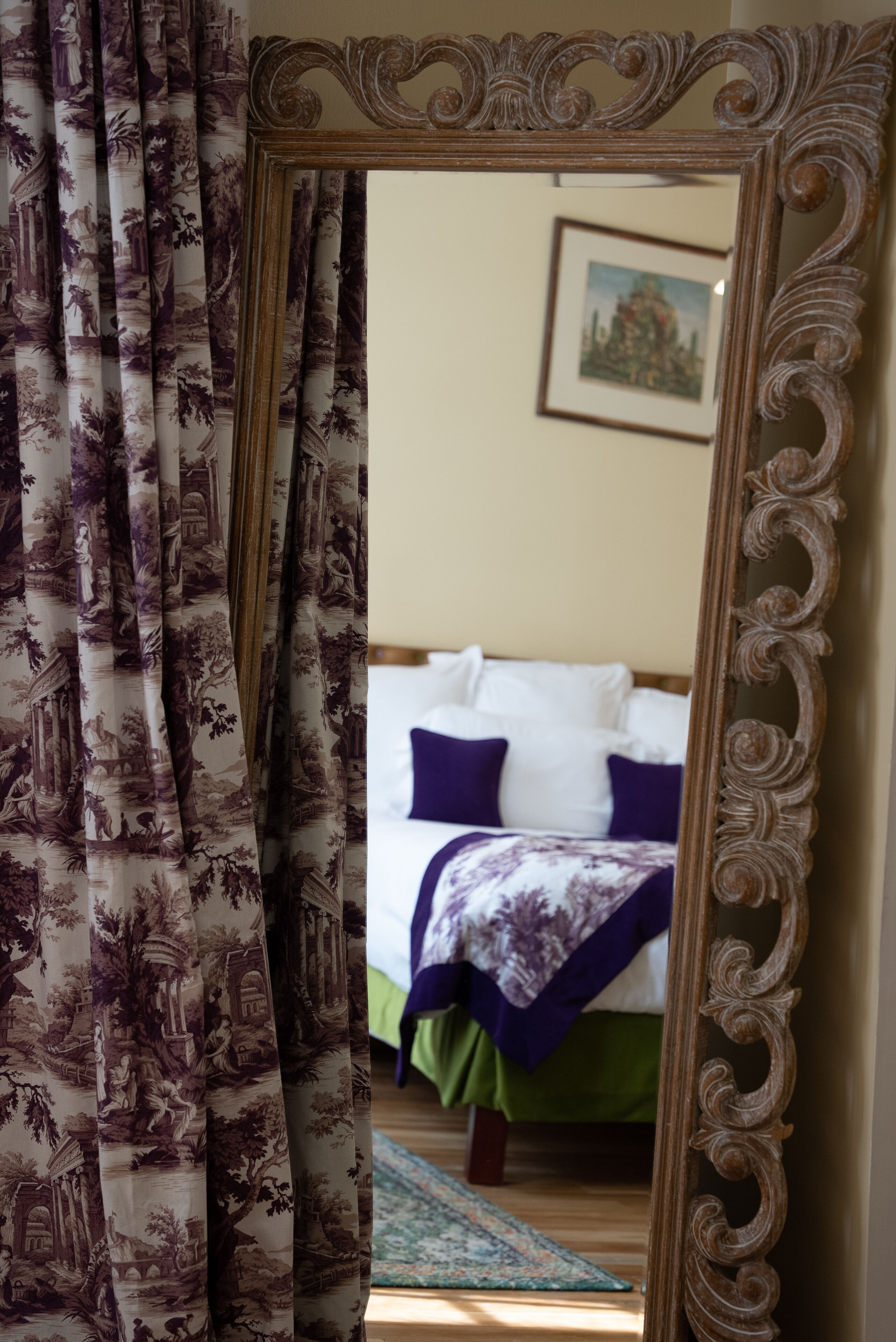 A bedroom with a bed, pillows, and a framed mirror reflecting the room.