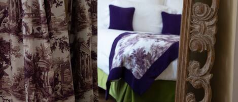 A bedroom with a bed, pillows, and a framed mirror reflecting the room.