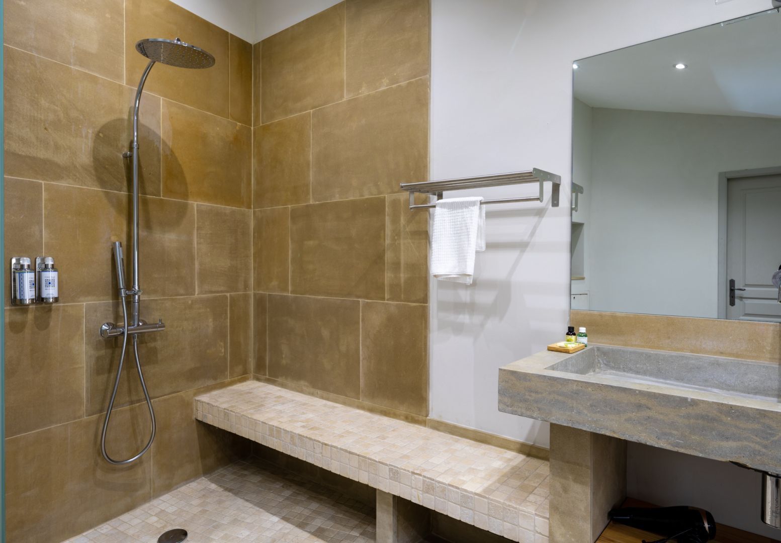 Une salle de bain équipée d’une douche, d’un banc, d’un lavabo et d’un miroir.