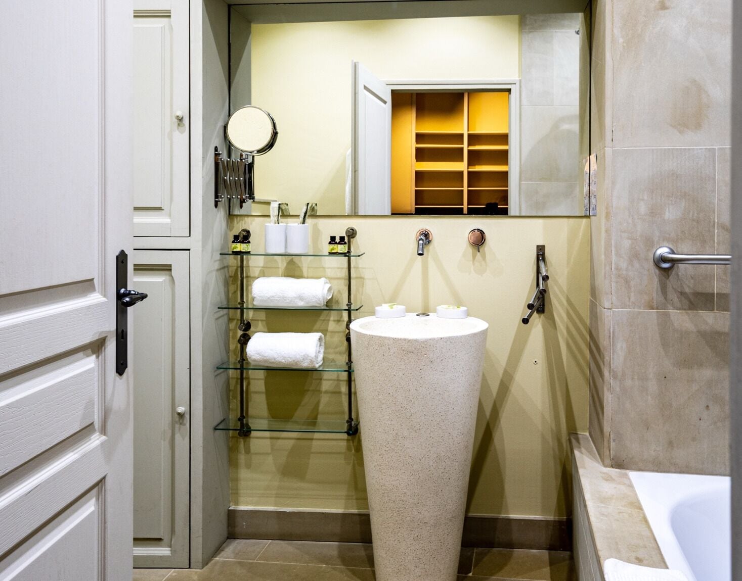 Une salle de bain avec un lavabo sur pied, une étagère en verre avec des serviettes, un miroir et un espace douche.