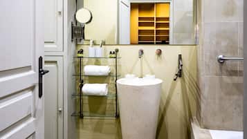 A bathroom with a freestanding sink, a glass shelf with towels, a mirror, and a shower area.
