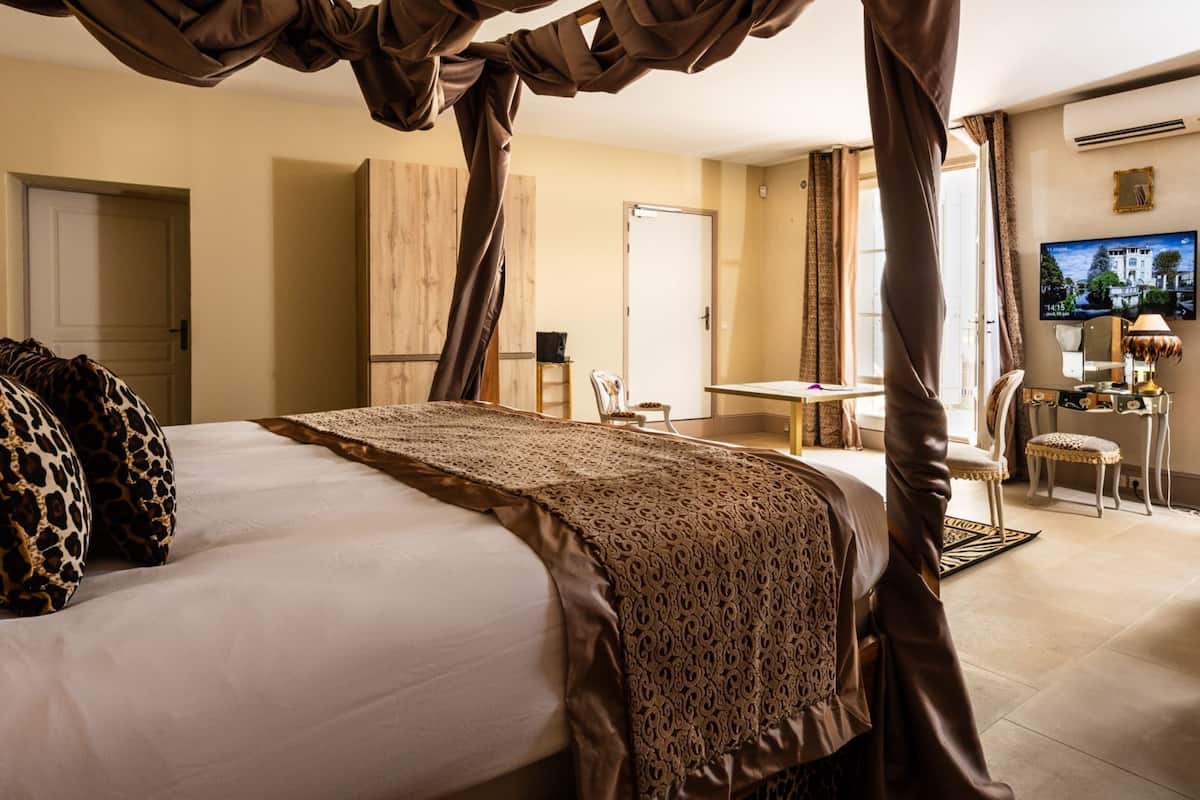 A hotel room with a large bed, a desk, a chair, a television, and a wardrobe.