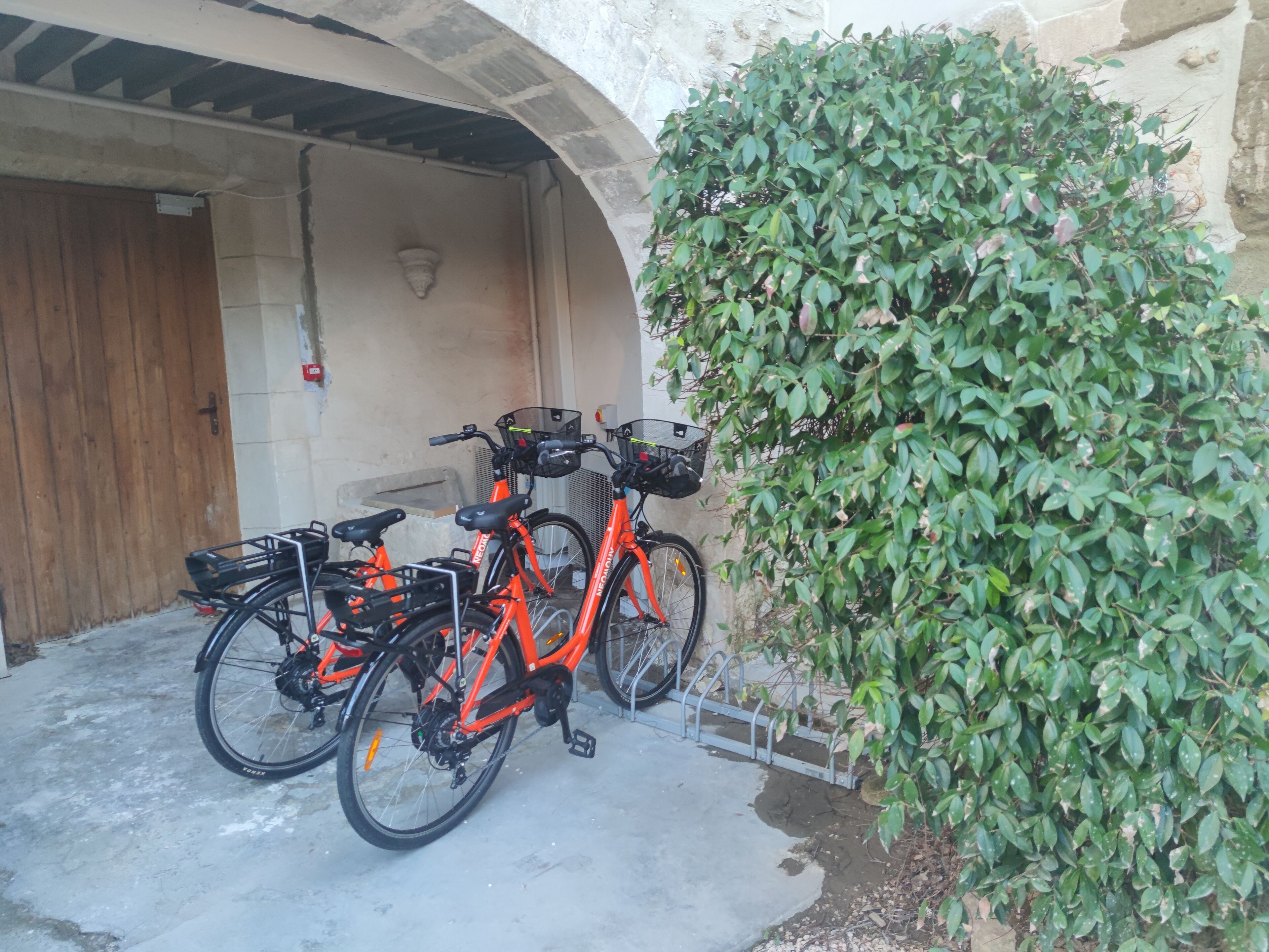 Una bicicleta estacionada bajo un arco de piedra con una puerta de madera y una lámpara en la pared.