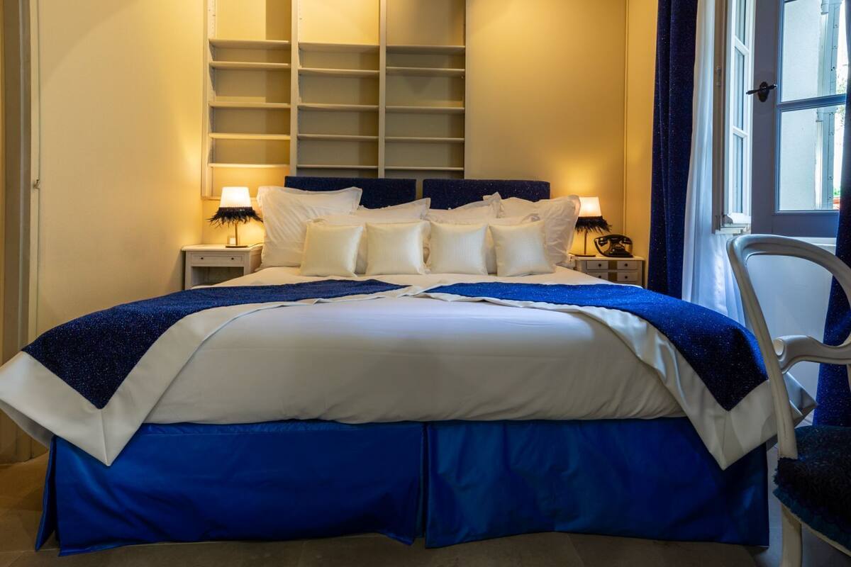 A neatly made bed with a blue and white bedspread, two bedside lamps, and a chair to the right.
