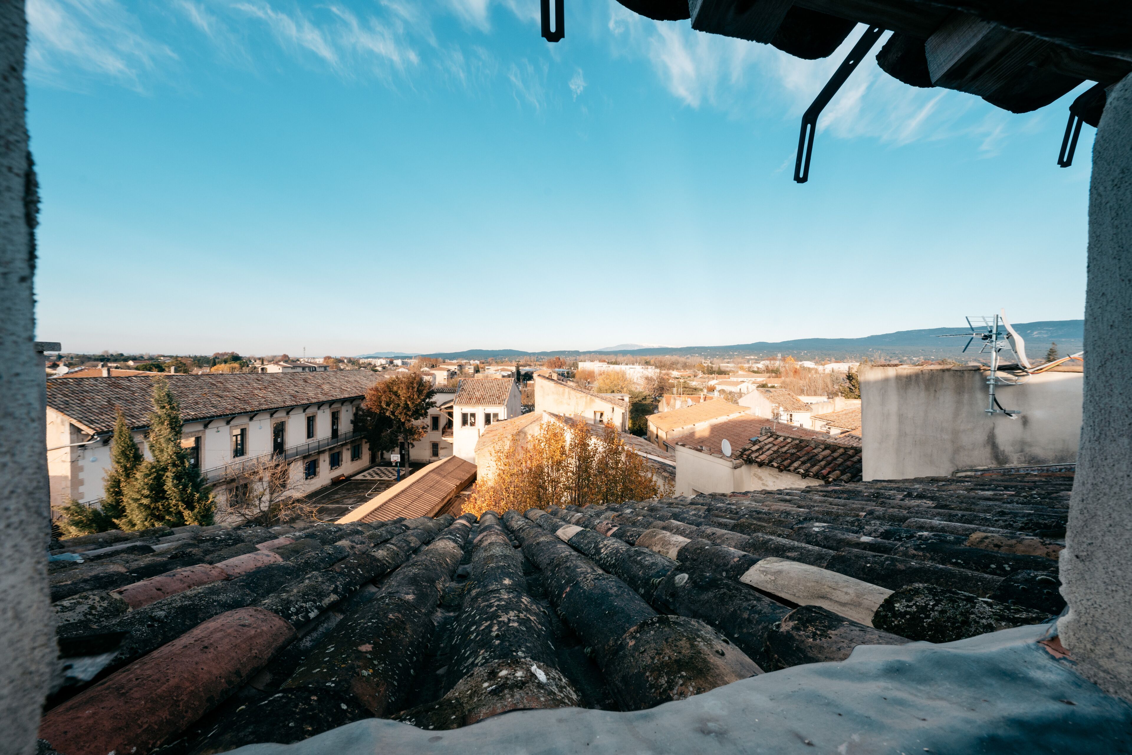 Vue depuis une terrasse sur le toit, avec un ciel dégagé, présentant des bâtiments traditionnels aux toits de tuiles et un mélange de styles architecturaux.