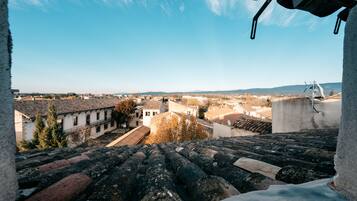 Vue depuis une terrasse sur le toit, avec un ciel dégagé, présentant des bâtiments traditionnels aux toits de tuiles et un mélange de styles architecturaux.