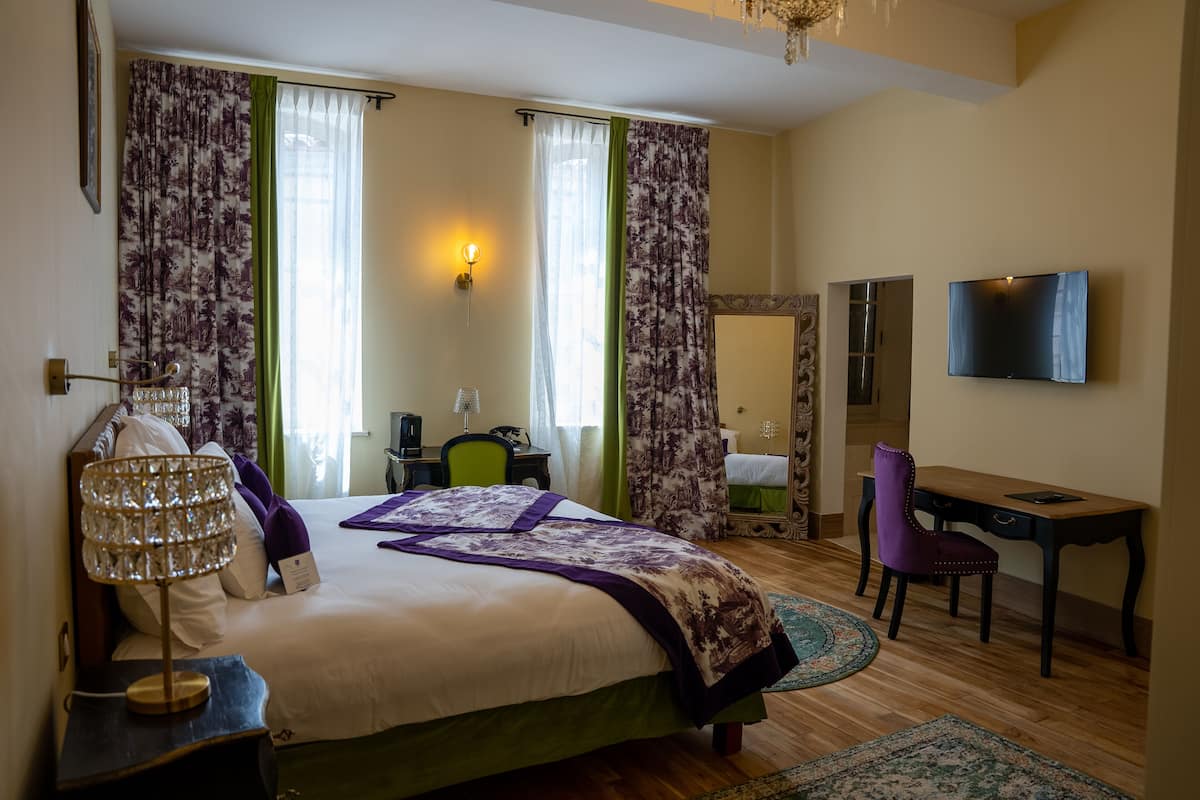 A bedroom with a bed, a desk, a chair, a TV, and a mirror.