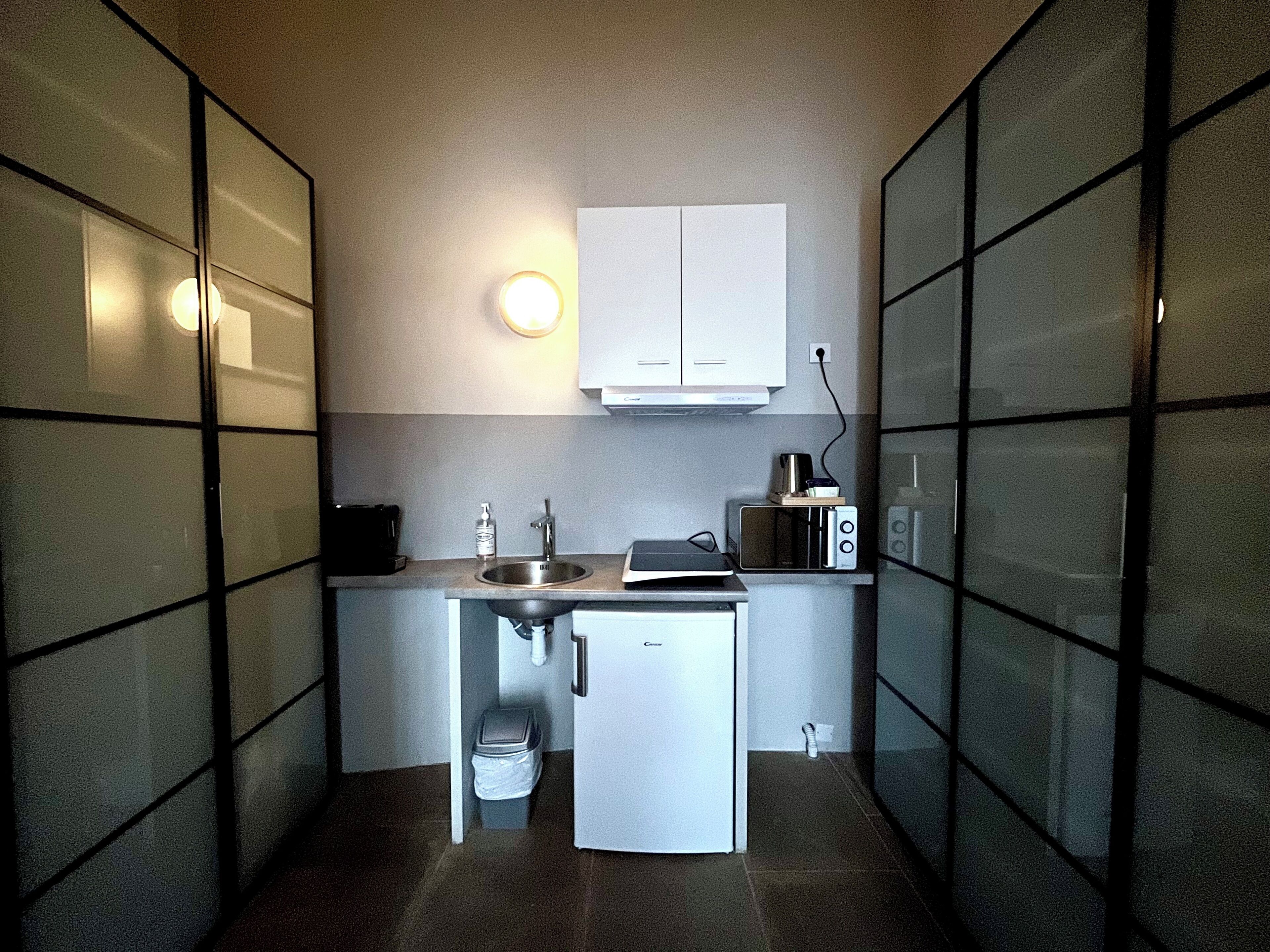A compact kitchenette with a sink, a small refrigerator, a microwave, and a cabinet above the counter.