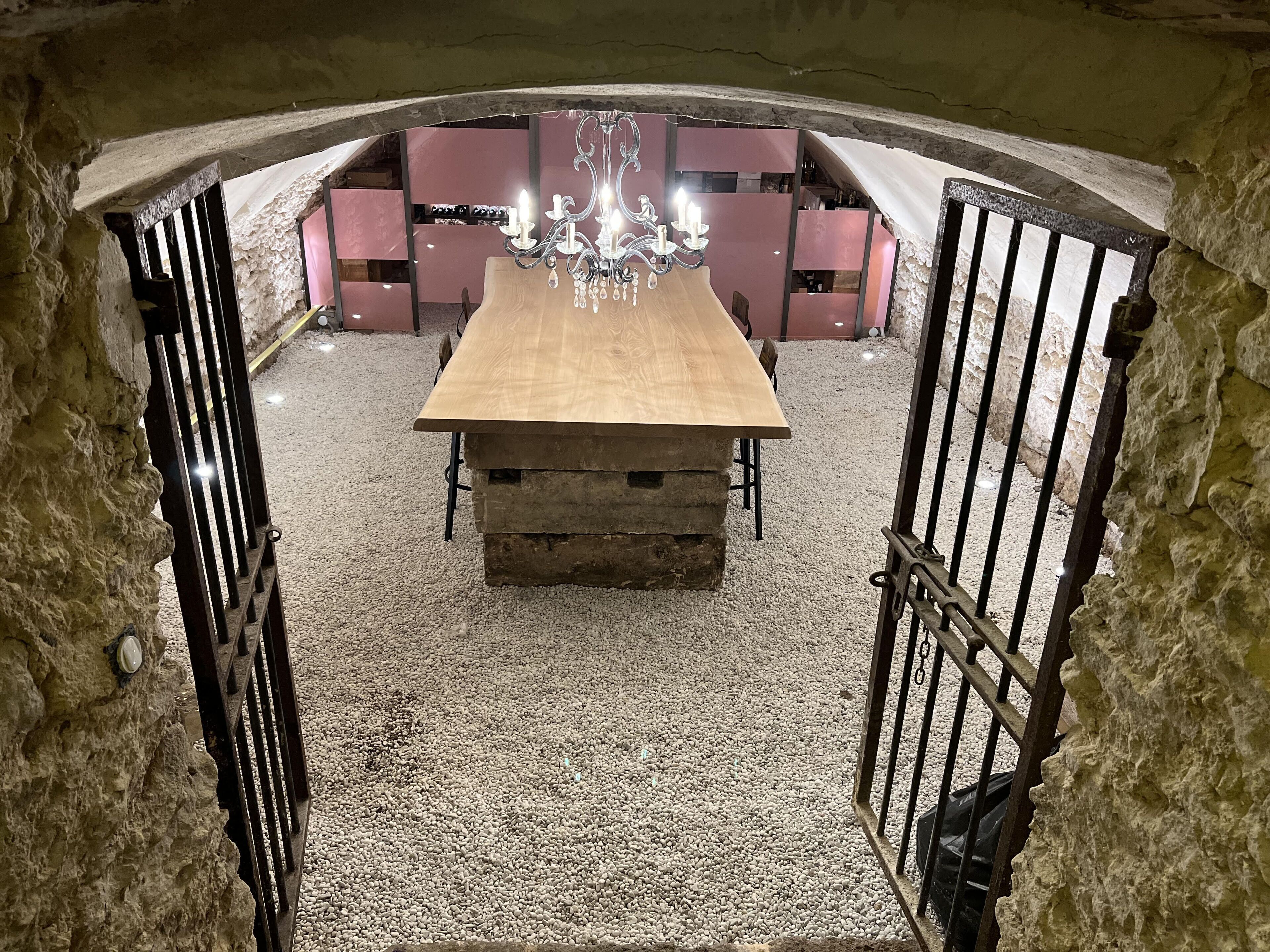 A rustic stone archway leading to a dining area with a wooden table and chairs, a chandelier, and a stone wall.