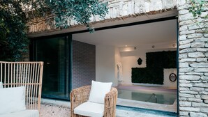 A wicker chair with a white cushion outside a building with a stone facade and a glass door. - Le Clos Violette D'Aglaé (L'Isle-sur-la-Sorgue)