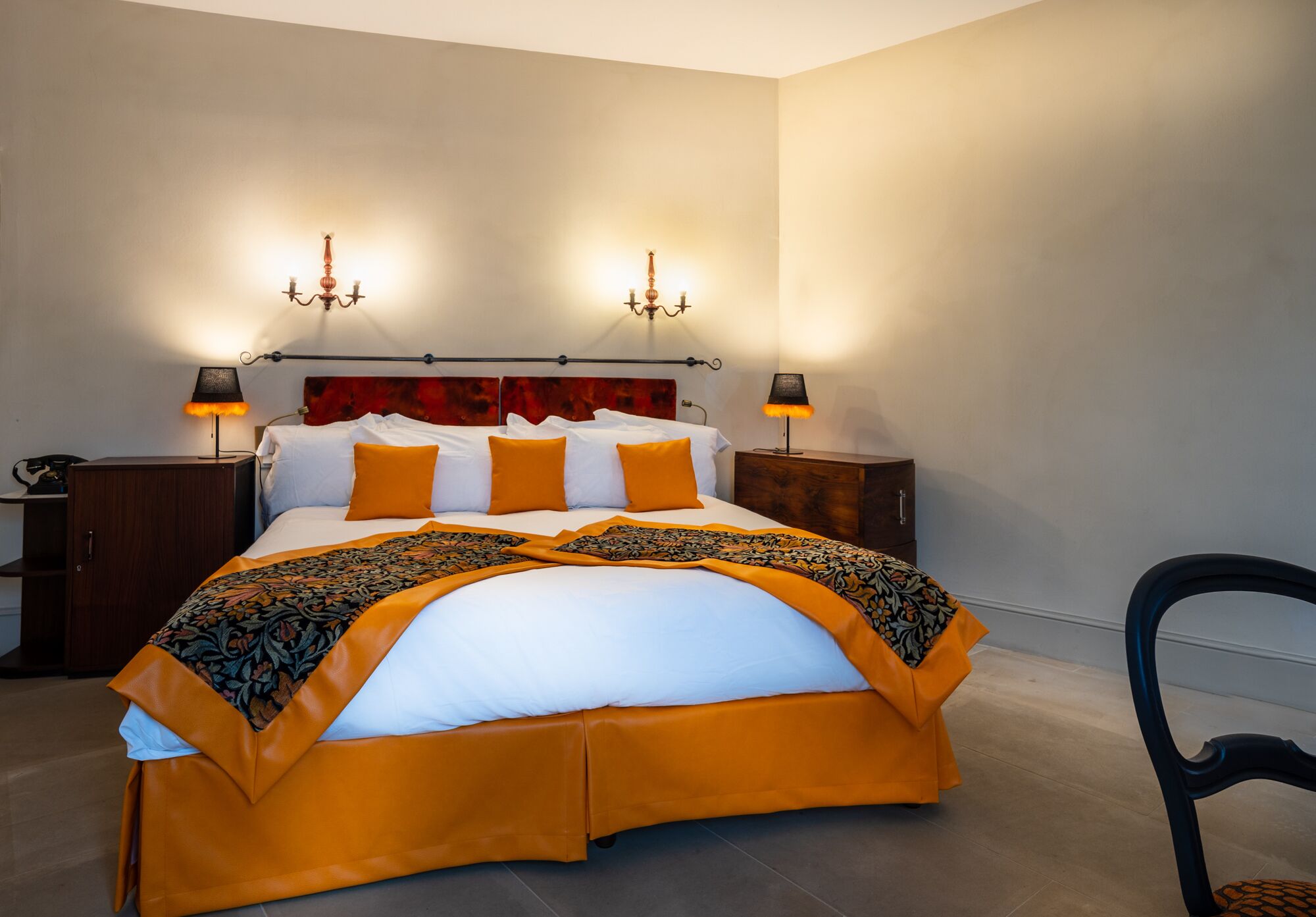 Un lit bien fait, avec une couvre-lit blanche et orange, deux lampes de chevet et une tête de lit rouge.