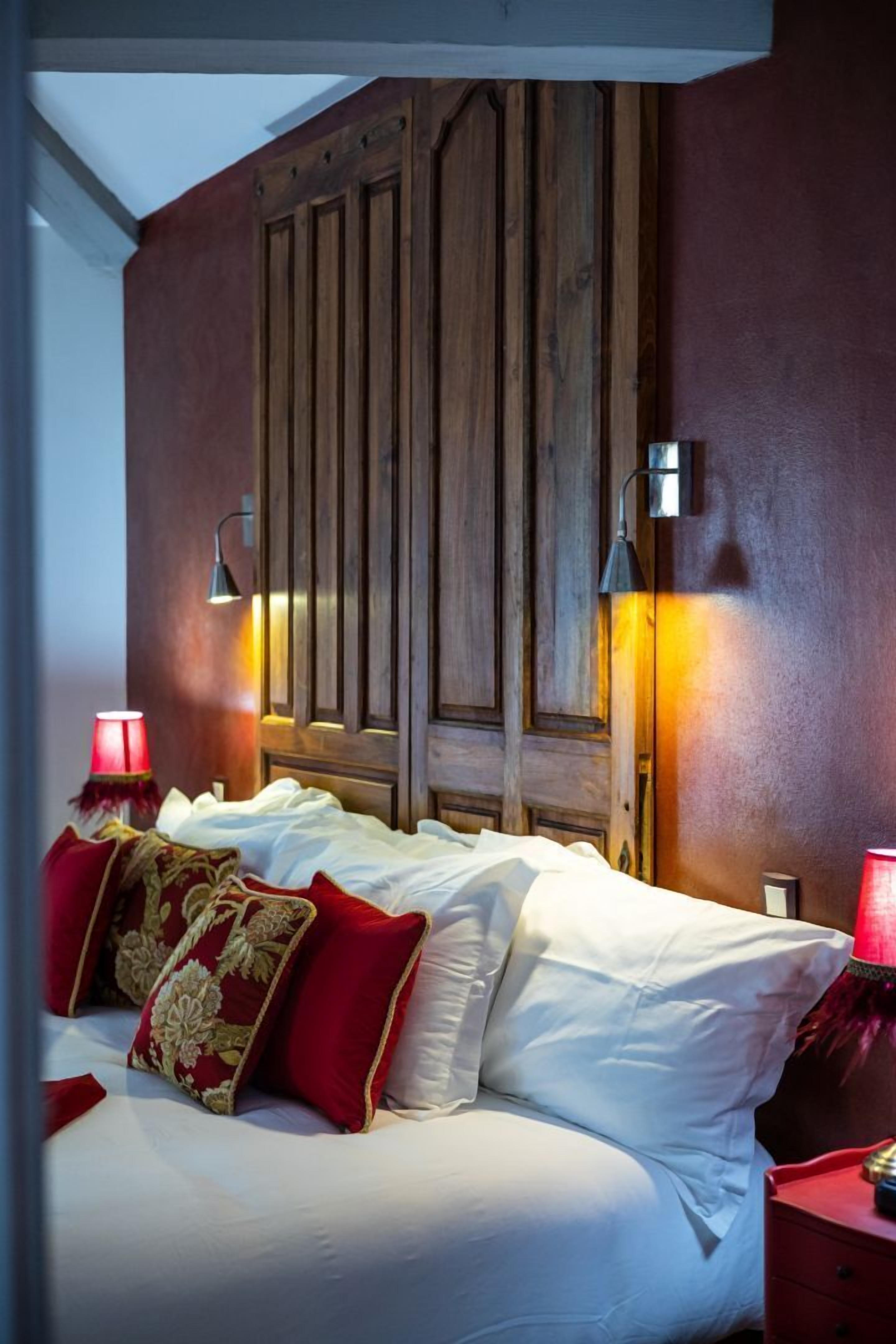 Une chambre à coucher avec une tête de lit en bois, du linge de lit blanc et des coussins rouges.