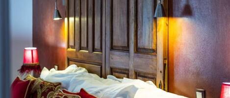 A bedroom with a wooden headboard, white bedding, and red pillows.