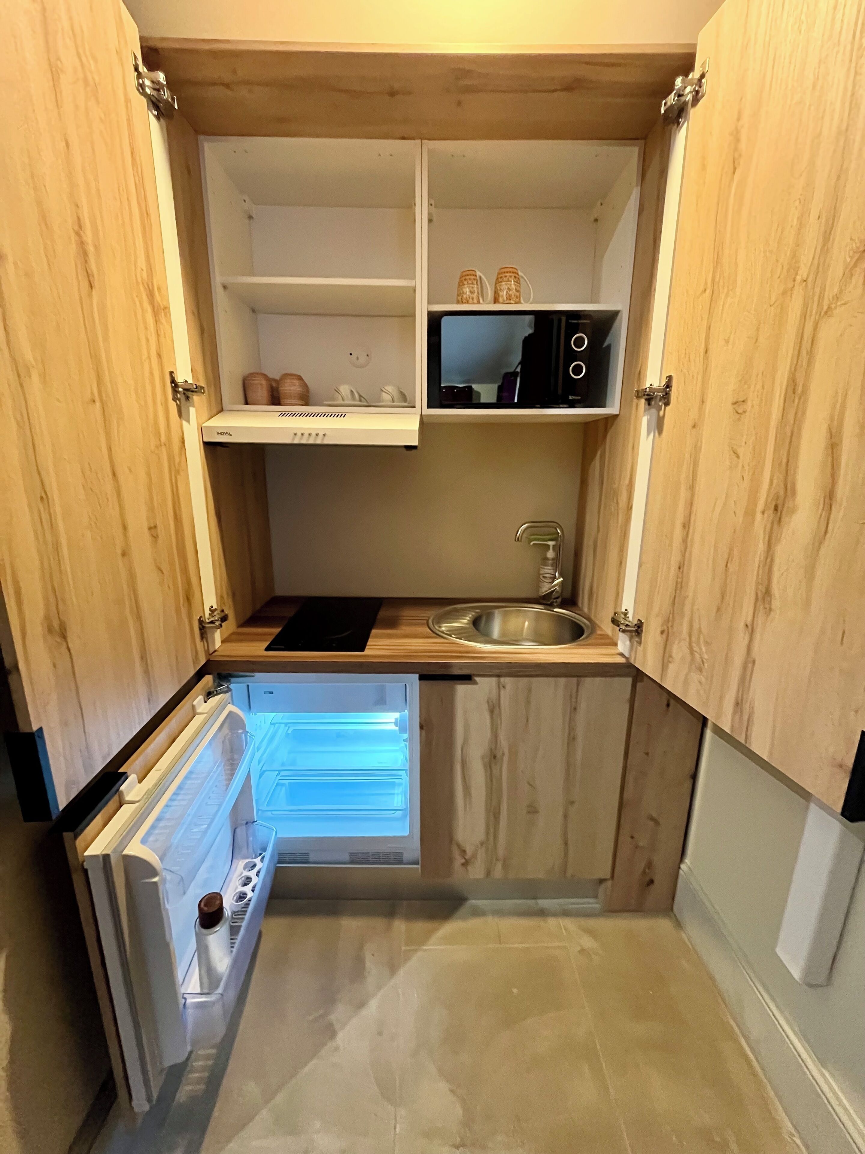 Una cocina compacta con armarios de madera, microondas integrado, lavabo y refrigerador.