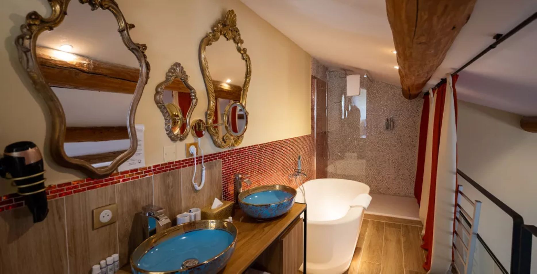 Une salle de bain avec un meuble-lavabo en bois, une baignoire blanche et un grand miroir doté d’un cadre orné.