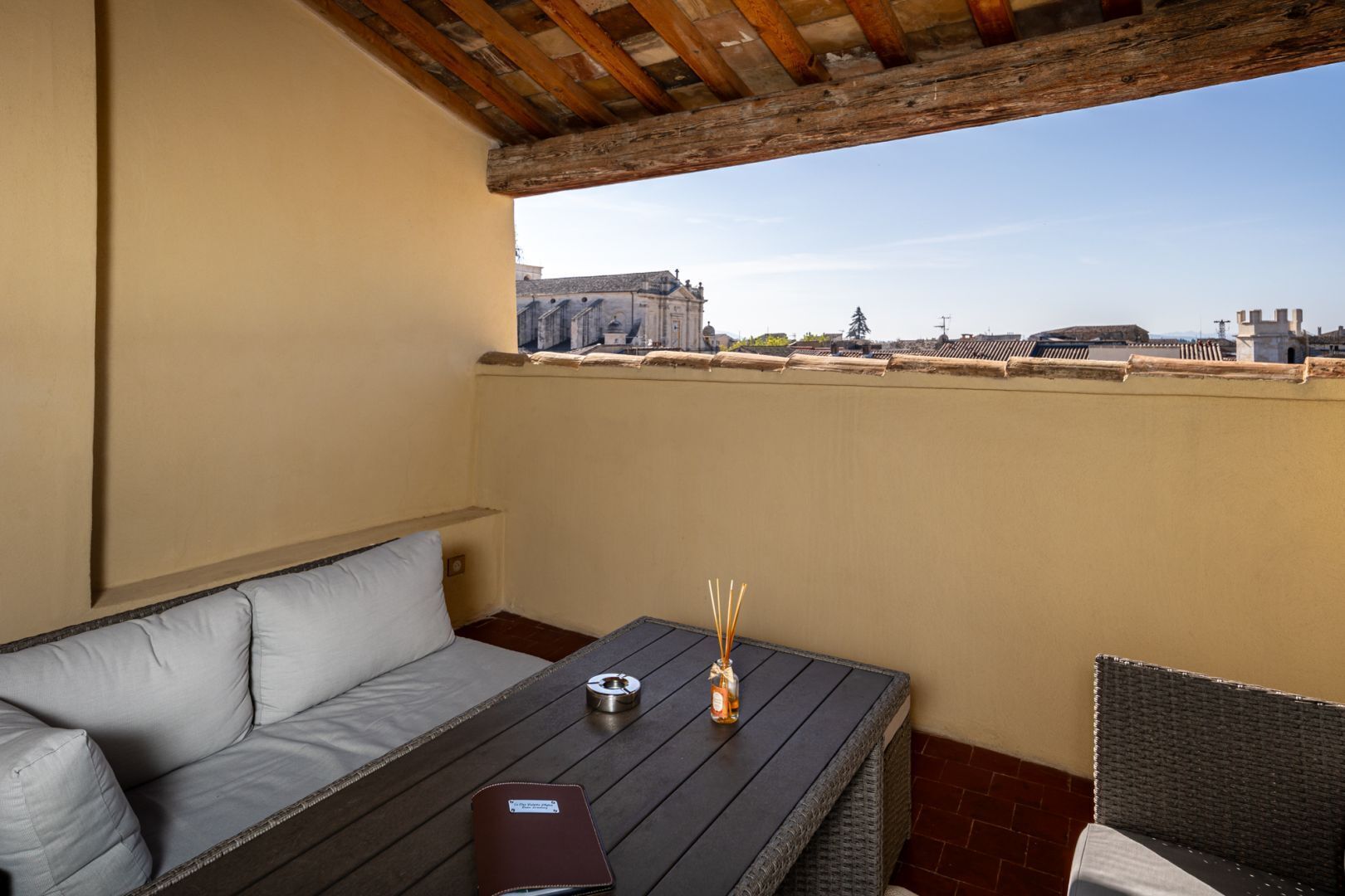 A rooftop terrace with a sofa, a small table, and a wicker chair.