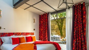A modern bedroom with a large bed, red and white bedding, and a view of a garden through a glass door. - Le Clos Violette D'Aglaé (L'Isle-sur-la-Sorgue)