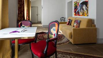 Een woonkamer met een bank, een eettafel met stoelen, een schilderij aan de muur en een kamerbreed tapijt.