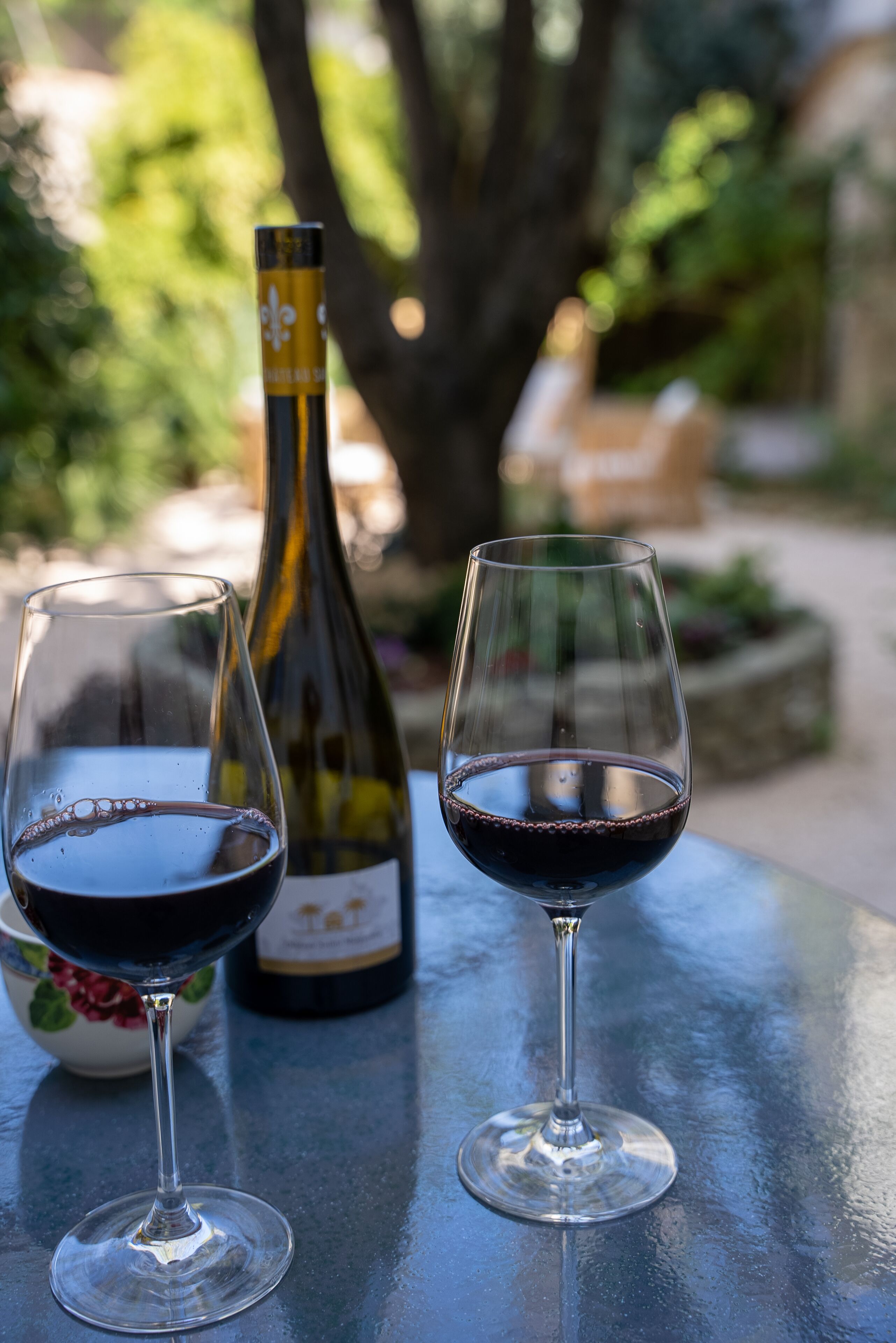 Two wine glasses on a table with a bottle of wine in the background.