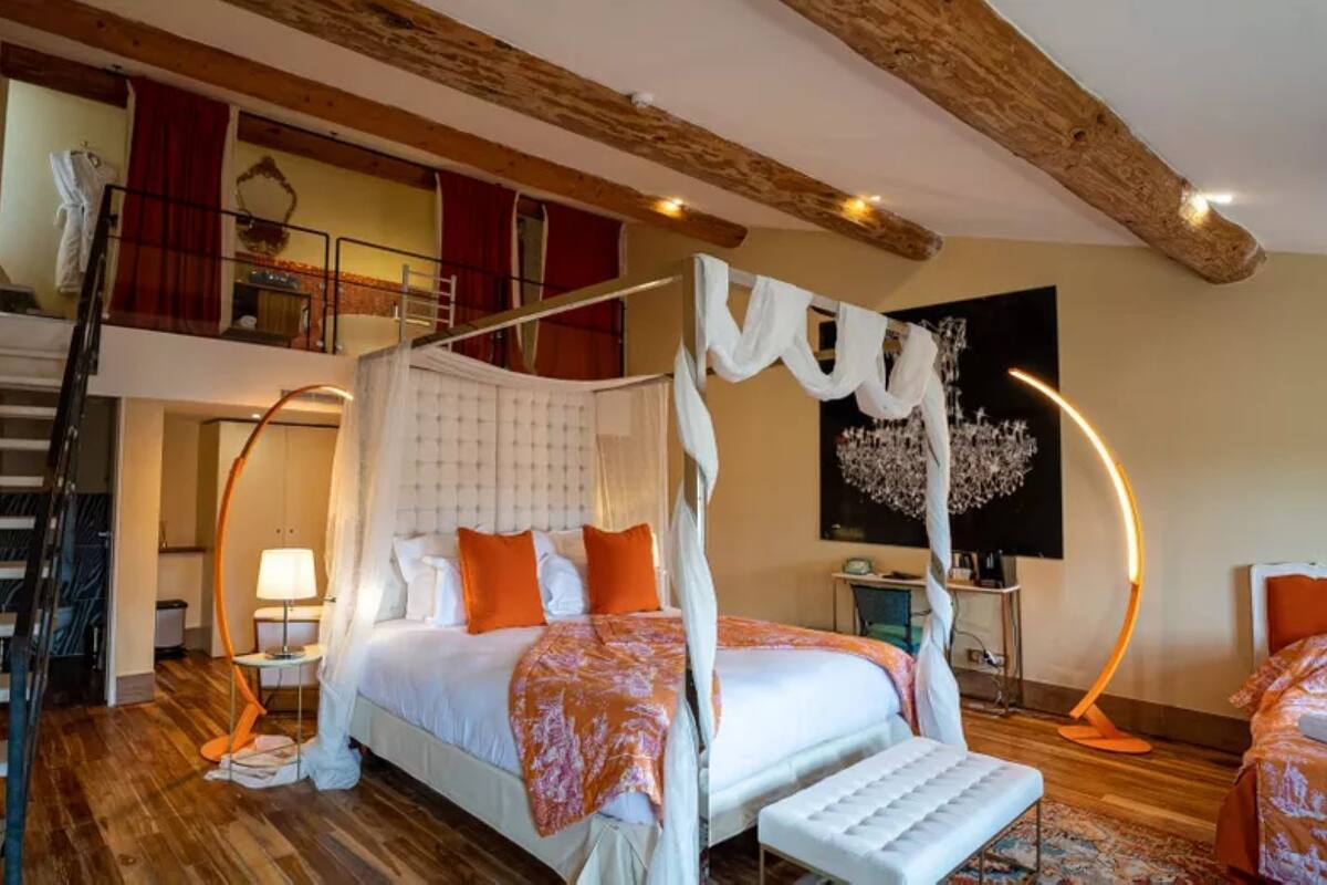 A four-poster canopy bed with a wooden staircase and a second-level balcony in a hotel room.