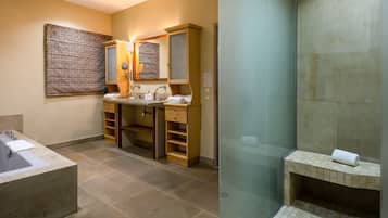 Une salle de bain dotée d’une grande baignoire, de deux vasques avec des meubles en bois, et d’une douche séparée par des parois en verre.
