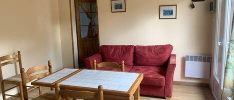 Un comedor con una mesa y sillas de madera, un sofá rojo y una ventana con persianas.