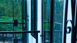 Uma varanda com guarda-corpo de metal, vista para árvores e fachada de um edifício.