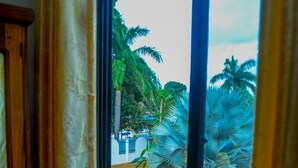 Janela com vista para um jardim com palmeiras e um banco.