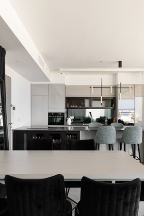 A modern kitchen with a central island, dark cabinetry, and a dining area with a white table and black chairs. - Luxury with Terrace & Sea View by FeelHome (Tel Aviv)