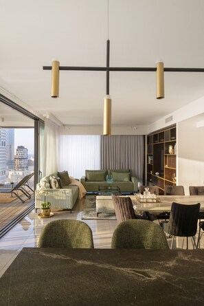 A modern living room with a green sofa, a dining table, and a city view through large windows. - Luxury with Terrace & Sea View by FeelHome (Tel Aviv)