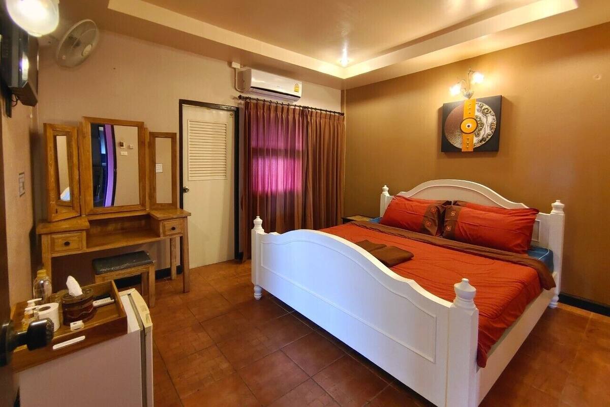 Une chambre à coucher avec un lit blanc, des rideaux marron, une commode en bois, un miroir et un climatiseur fixé au mur.