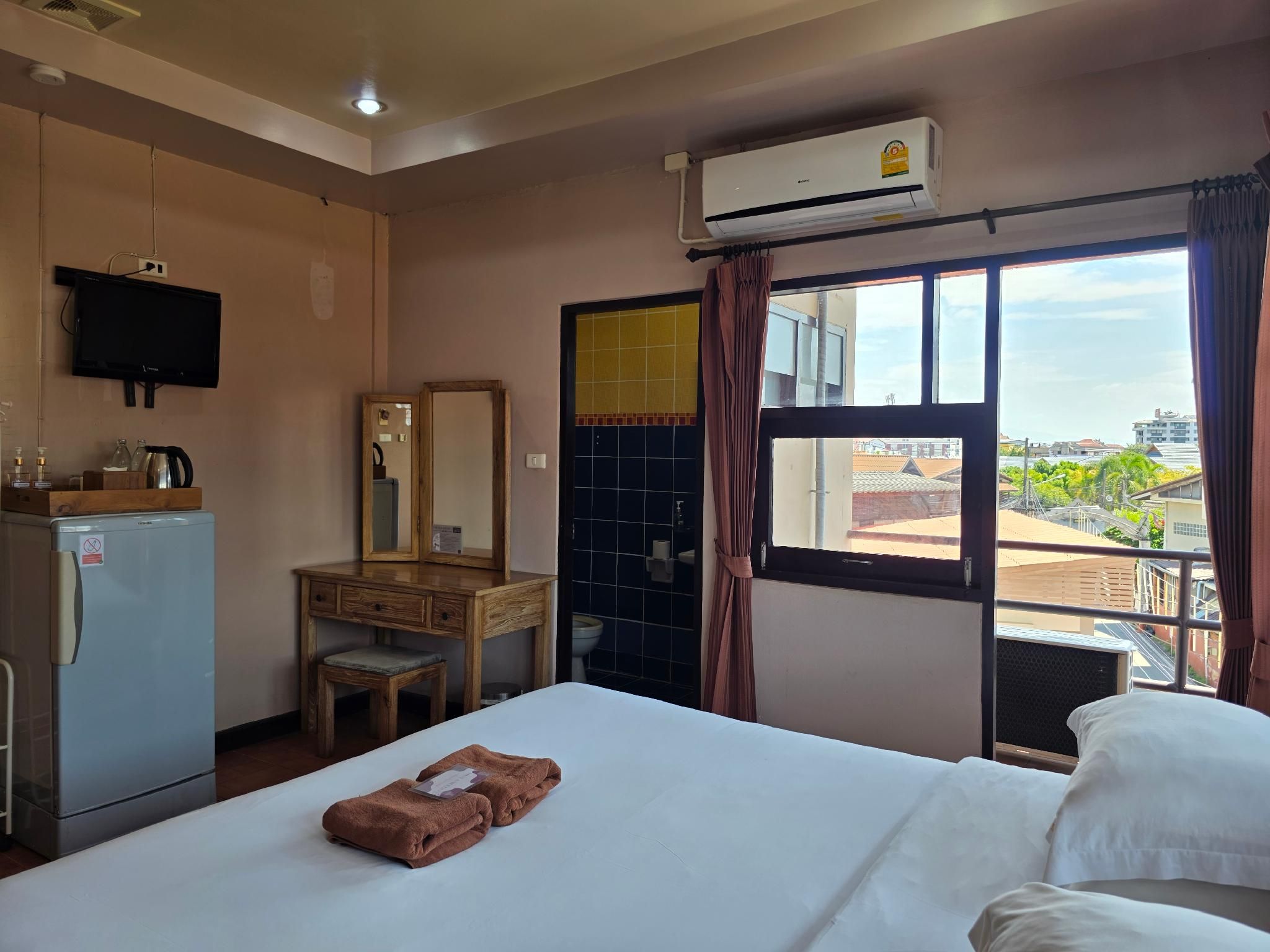 A hotel room with a bed, a desk with a mirror, a television, and an air conditioning unit.