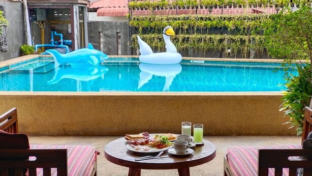 A pool with a swan float, a dining table with breakfast, and a view of a building with plants. - Wualai Boutique by Lanna Oriental (Chiang Mai)