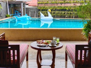 A pool with a swan float, a dining table with breakfast, and a view of a building with plants. - Wualai Boutique by Lanna Oriental (Chiang Mai)