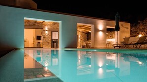 Una piscina con reflejo claro, un muro de piedra y un área de descanso con sillas y una mesa.