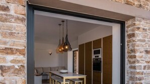 Una cocina moderna con una isla central, un comedor con sillas de madera y una pared de piedra.