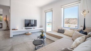 Een moderne woonkamer met een flatscreen televisie, een bank, een salontafel en een groot raam met uitzicht op het omliggende landschap.