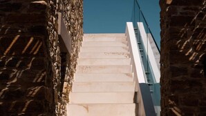 Una scala con pareti in pietra e ringhiera in metallo, che sale verso l'alto.
