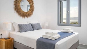 Une chambre à coucher avec un lit, un miroir rond, une fenêtre donnant sur un beau paysage et une table de chevet avec une lampe.