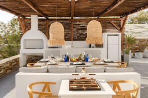 Un espacio exterior para comer con una pared de piedra, una pérgola de madera y una cocina exterior blanca.