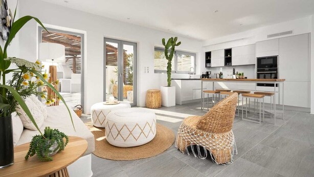 Un salon moderne avec un canapé, des poufs, un fauteuil en osier et un coin repas doté d’un bar.