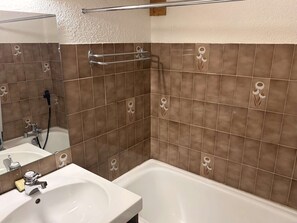 A bathroom with a white sink, a mirror, a shower, and brown tiled walls with floral patterns.